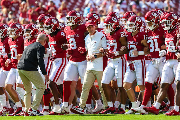 Brent Venables and the Oklahoma football team walk in a group with their arms linked